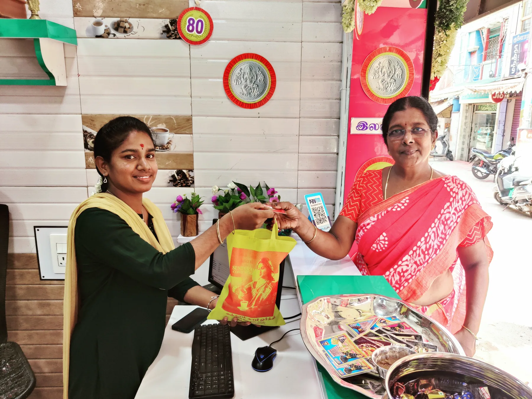 A Sundaram Coffee Works bag handed across the counter to a customer in a red sari
